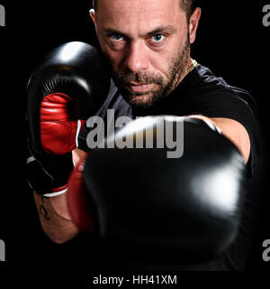 Portrait de l'athlète masculin de l'homme boxer à agressif avec des gants de boxe sur chemise noire, et des tatouages. Isolé sur fond noir Banque D'Images