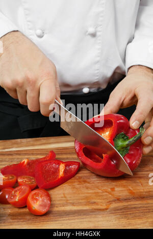 Photo d'un chef chopping un poivron rouge sur une planche à découper en bois. Banque D'Images