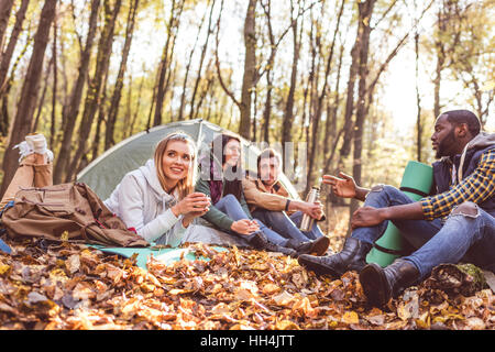 Jeunes amis voyageurs assis et parler près de tente en forêt d'automne Banque D'Images