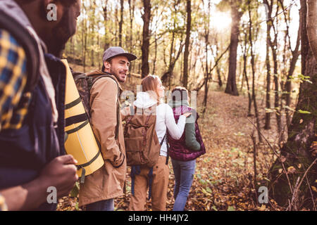 Quatre jeunes backpackers marcher dans la rangée en forêt d'automne au coucher du soleil Banque D'Images