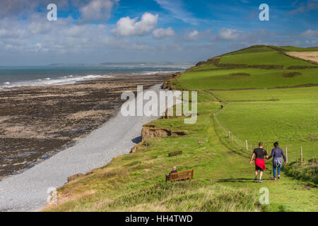 Un couple marche le long de la South West Coast Path, à l'égard Westward Ho !, comme le soleil illumine le sentier. Banque D'Images