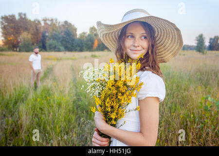 Belle femme holding bouquet de fleurs jaunes et à la recherche à l'appareil photo avec son petit ami sur l'arrière-plan. Banque D'Images