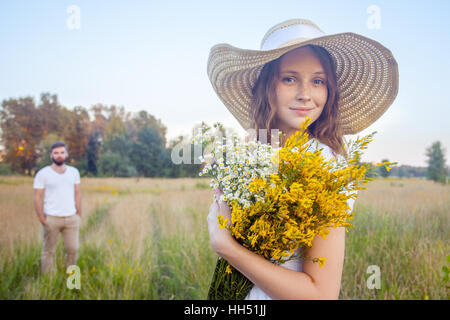 Belle femme holding bouquet de fleurs jaunes et à la recherche à l'appareil photo avec son petit ami sur l'arrière-plan. Banque D'Images