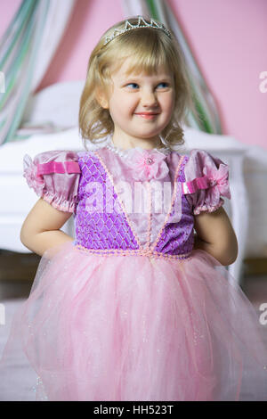 Peu heureux princess fille en robe rose et couronne dans son prix pose et souriant. Banque D'Images