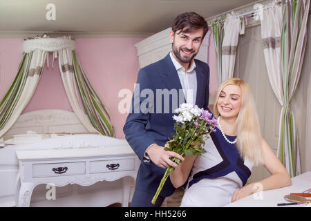 Jeune homme séduisant surprenant sa belle copine et lui donne son bouquet de fleurs blanc violet. Banque D'Images