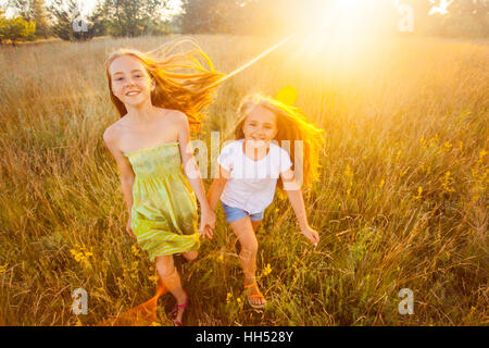 Deux belles sœurs s'exécutant sur la pelouse dans le parc naturel de l'outdoor en été. La liberté et l'insouciance. Enfance heureuse. Banque D'Images