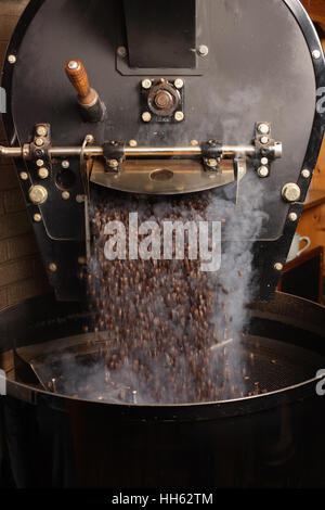 Photo de grains de café fraîchement torréfié provenant d'un grand torréfacteur de café est versé dans le cylindre de refroidissement. Motion Blur sur les haricots. Banque D'Images