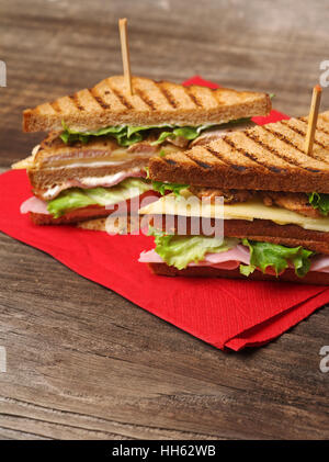 Photo d'un club sandwich fait avec la Turquie, bacon, jambon, tomates, fromage, laitue sur une serviette rouge et vieux bois table de pique-nique. Banque D'Images