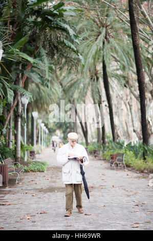 Malaga, Espagne. 18 Décembre, 2016. Homme de la marche et la lecture dans des jardins tropicaux luxuriants à Malaga, Andalousie, Espagne Banque D'Images