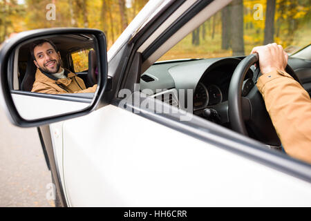 Homme barbu souriant reflétée dans un miroir de voiture en forêt d'automne Banque D'Images