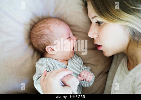 Belle jeune maman avec bébé fils lying on bed Banque D'Images