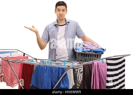 Guy confus tenant un panier de blanchisserie et des gestes avec sa main derrière un rack de vêtements cheveux isolé sur fond blanc Banque D'Images