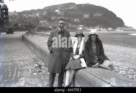 Années 1920, historique, un homme avec deux femmes souriant assis sur un mur de la mer, heureux d'être au bord de la mer Banque D'Images