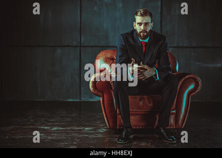 Young handsome businessman avec barbe en costume noir assis sur une chaise et de parler avec le président. Film rétro style couleurs effet. Banque D'Images
