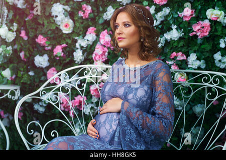 Jeune femme enceinte portrait dans jardin avec fleurs rose Banque D'Images