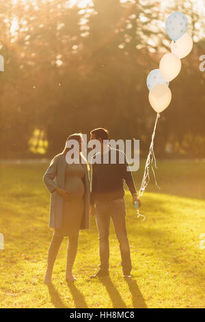 Jeune femme enceinte et man posing in autumn park avec des ballons dans la main Banque D'Images