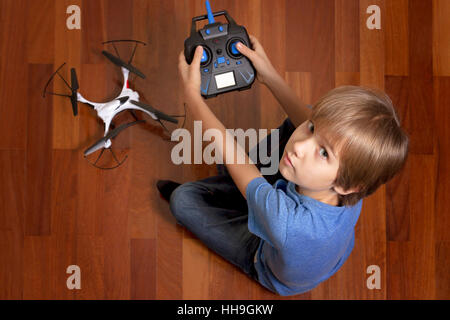 Petit enfant va jouer avec le drone quadcopter à la maison. Garçon assis sur le sol et tenant une télécommande radio Banque D'Images