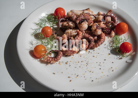 Frits dans l'huile d'olive, la pieuvre tentacules avec tomates cerises et épices servi sur plaque blanche Banque D'Images