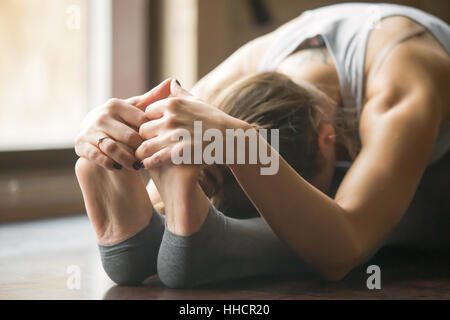 Jeune femme en paschimottanasana pose, arrière-plan, l'intérieur d'accueil Banque D'Images