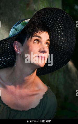 Tête-et-latéral sur l'épaule de black-haired femme d'âge moyen avec children's book classic Sun Hat résolution latérale vers le haut. Banque D'Images