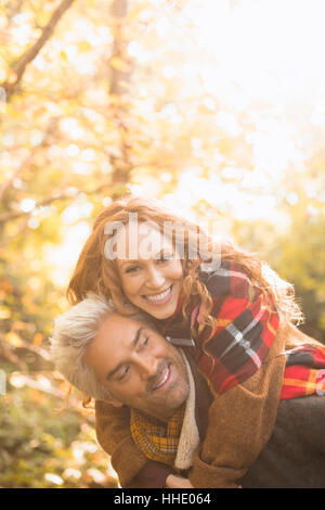 Portrait playful couple piggybacking en automne woods Banque D'Images