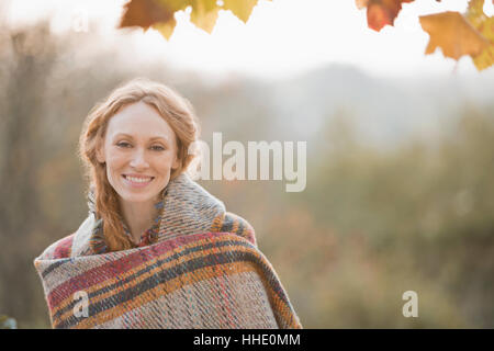 Portrait of smiling woman wrapped in blanket in autumn park Banque D'Images