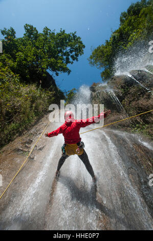 Un homme s'arrête pour tenir ses bras dans la chute de l'eau tandis que le canyoning, le Népal Banque D'Images