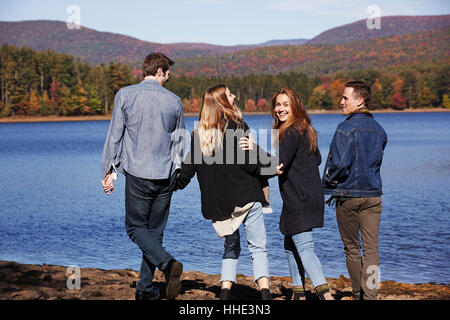Quatre personnes marcher le long, des couples main dans la main, sur la rive d'un lac. Banque D'Images
