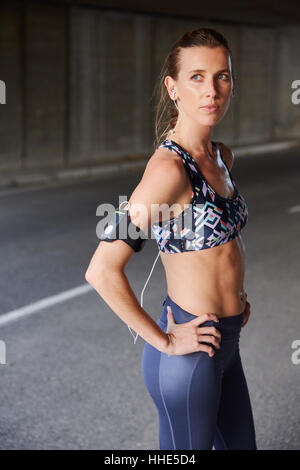 Mettre en place une coureuse en soutien-gorge de sport avec un lecteur mp3 et écouteurs brassard on urban street Banque D'Images