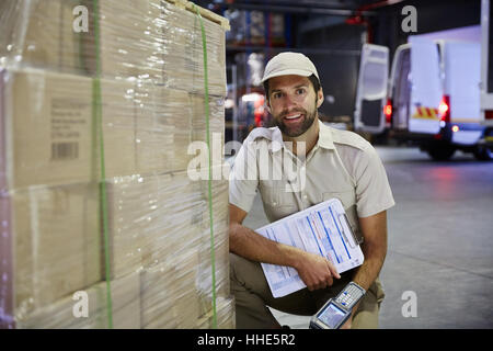 Portrait confiant camionneur travailleur avec scanner à palettes de cartons au quai de chargement de l'entrepôt de distribution Banque D'Images