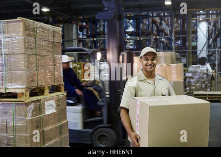 Portrait smiling worker carrying cardboard box au quai de chargement de l'entrepôt de distribution Banque D'Images