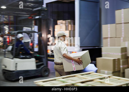 Les travailleurs et les boîtes en carton de chargement du chariot élévateur dans des camions au quai de chargement de l'entrepôt de distribution Banque D'Images