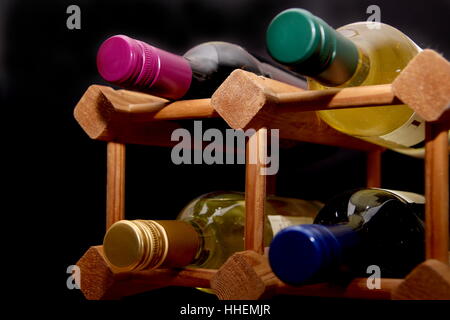 Différentes couleurs de robes de bouteilles de vin dans un casier à vin en bois sur fond noir Banque D'Images