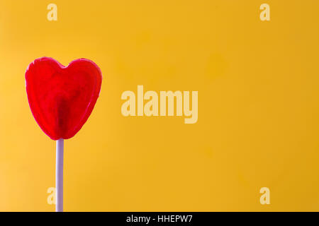 Sucette rouge en forme de coeur avec sur fond jaune. Concept d'amour. Le jour de la Saint-Valentin. Banque D'Images