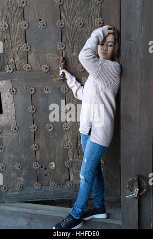 Fille à côté d'une vieille porte en bois. Tir vertical avec lumière naturelle. Banque D'Images