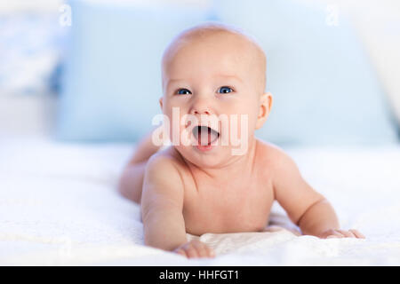 Bébé garçon vêtu de blanc à couches chambre ensoleillée. Le nouveau-né de se détendre dans le lit. Garderie pour les enfants. Textile et de la literie pour enfant Banque D'Images