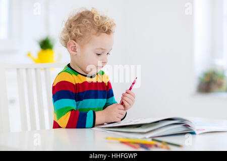 Cute little boy doing homework, lire un livre, des pages à colorier, écrire et peindre. Les enfants de la peinture. Attirer les enfants. Banque D'Images