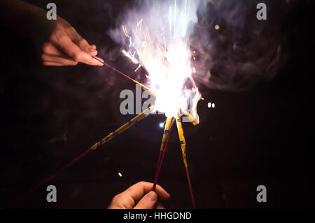 Close-up de mains qui s'unissent pour enflammer les étinceleurs (fireworks) lors d'une soirée de célébration. Banque D'Images