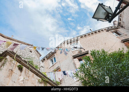 À la recherche jusqu'à des bâtiments en pierre dans la vieille ville de Trogir, Croatie. Blanchisserie pend d'une fenêtre à l'autre et il y a un réverbère. Banque D'Images