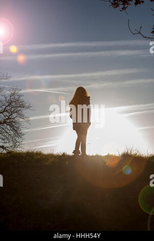 Silhouette d'une vue arrière d'un seul femme méconnaissable par un banc dans un endroit calme avec un soleil ciel et les arbres. Banque D'Images