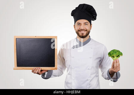 Souriante jeune chef avec tableau noir en blanc et le brocoli dans la main Banque D'Images