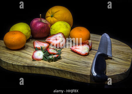 Les fraises coupées avec d'autres fruits sur une planche à découper. Banque D'Images