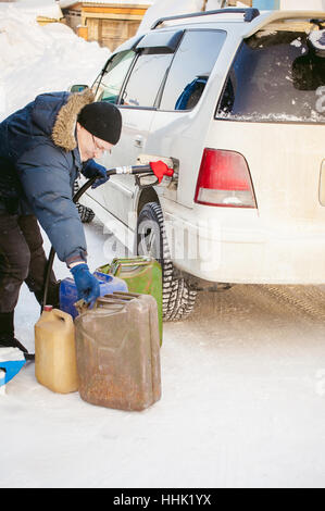 Homme adulte remplit une voiture avec l'essence à une station essence en hiver. l'homme de la buse de ravitaillement en tenant à la main, verser le liquide dans le canister et fu Banque D'Images