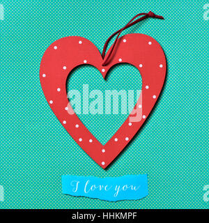 Un ornement en forme de cœur rouge à motifs de points blancs et un morceau de papier bleu avec le texte je t'aime écrit en C, sur un fond bleu, Banque D'Images