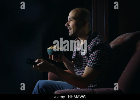 Guy regarder la TV avec télécommande à la maison la nuit Banque D'Images