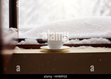 Mug avec thé et café sur le rebord de la fenêtre de la neige en hiver w Banque D'Images