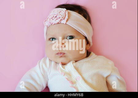 Portrait of a deux mois cute baby girl Fleur dentelle bandeau et couché sur une couverture rose Banque D'Images