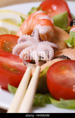 Une salade de fruits de mer avec des légumes close up sur une assiette avec des baguettes. vertical. Banque D'Images