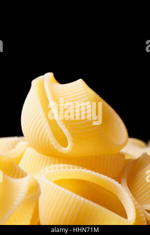 Macaroni italien non cuites lumaconi sur fond noir vertical close up Banque D'Images