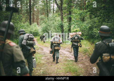 Groupe d'interprètes historiques non identifiés habillés en soldats allemands marchant le long de la route forestière. La saison d'été. Banque D'Images